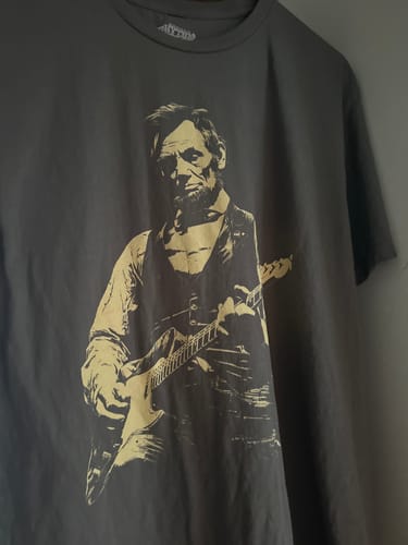 Customer's dark grey Lincoln Guitar T-Shirt with a graphic of Abraham Lincoln playing an electric guitar.