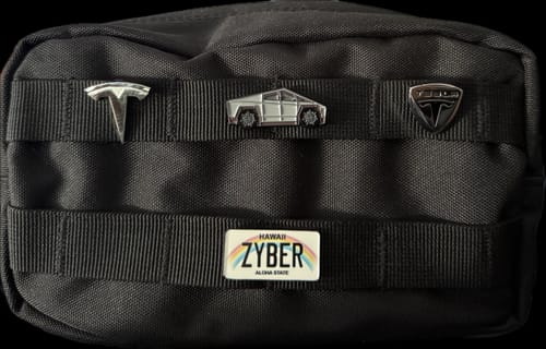 Customer's Hawaii License Plate Enamel Pin, customized with 'ZYBER', attached to the front of a black utility bag with other pins.