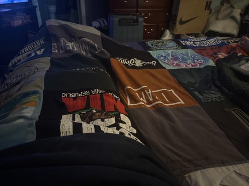 Customer's Project Repat T-Shirt Quilt, featuring colorful shirt patches, spread across a bed in a bedroom.