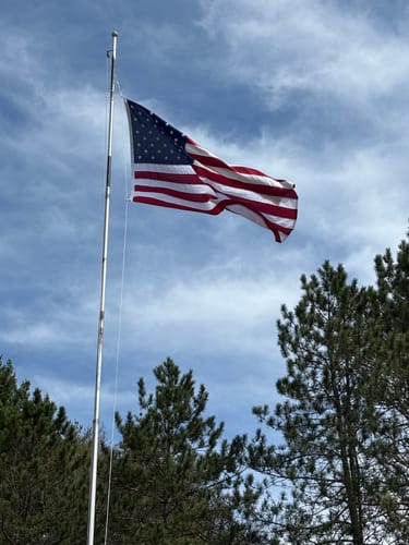 Customer's Ultra Heavy Duty American Flag waving on a flagpole against a cloudy blue sky.