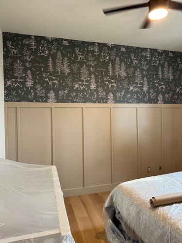 Customer's room showing dark Gunnison Wallpaper with a woodland pattern above tan board and batten.
