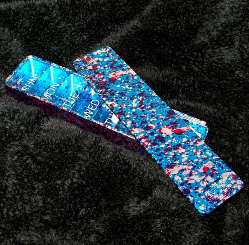 Reviewer's open Weekly Case with a blue and red splatter pattern, showing the labeled daily compartments inside.