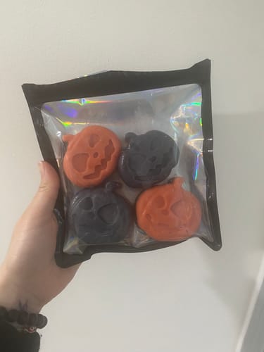 Reviewer holding a clear bag showing four orange and black pumpkin-shaped wax melts.