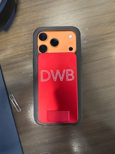 Customer's red metal pill case, personalized with 'DWB' initials, on the back of a phone.