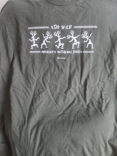 Customer's close-up of the wrinkled, dark green Stay Wild Petroglyphs Tee, showing the white petroglyph graphic.
