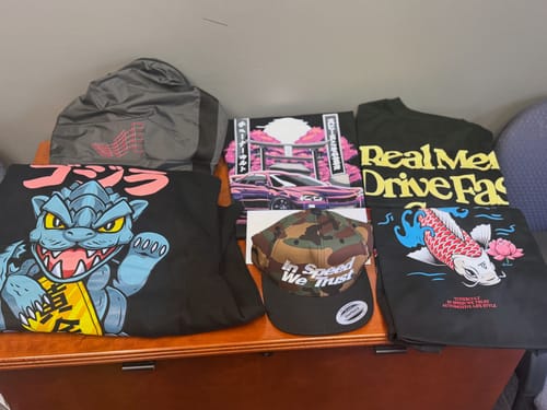 Customer displays their CULTIMATE MYSTERY CASH BOX contents, including graphic shirts, outerwear, and a hat.