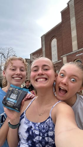 Three smiling reviewers taking a selfie outside, one holding a Cael's Cookie package while another makes a funny face.
