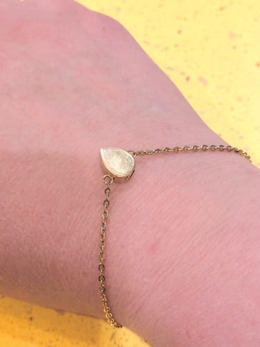 Close-up of a reviewer wearing the delicate, gold-colored Teardrop Urn Bracelet on their wrist.
