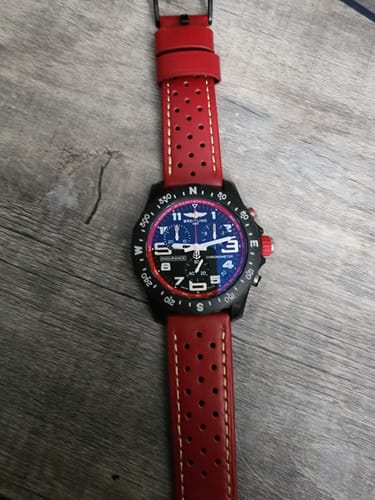 Reviewer's red Leather Sport Grip strap with tan stitching, shown on a black Breitling watch against a wood background.