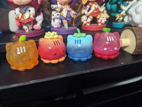 Reviewer's four colorful Octcats' Fruit Market figures lined up on a cluttered desk.