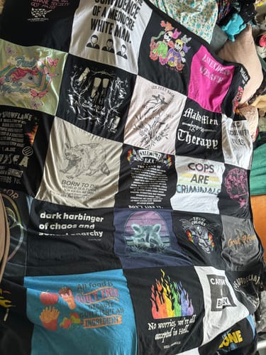 Customer's full-size Project Repat T-Shirt Quilt made from various activist-themed t-shirts spread across a bed.
