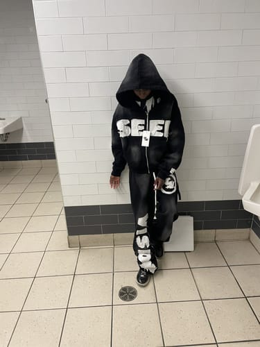 Customer wearing the black SEEK VISIONZ SET hoodie and pants in a tiled room.