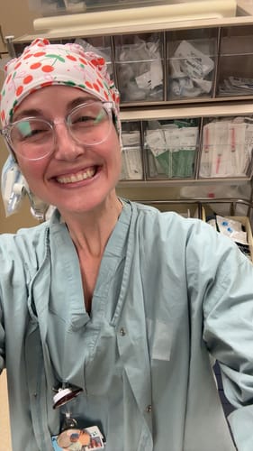 Reviewer smiling in a medical setting while wearing the DuoStyle Scrub Hat with a cute cherry pattern.