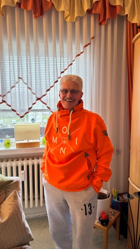 Kunde lächelt in seinem leuchtend orangefarbenen Moin Schalkragen Sweatshirt.