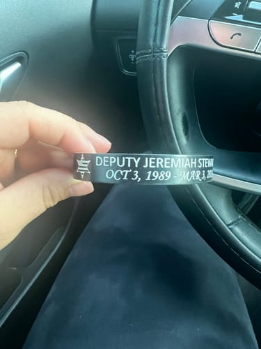 Close-up of a reviewer's hand holding a customized black memorial bracelet with an engraved name and sheriff badge.