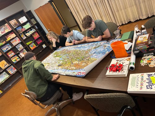 Reviewer and family gathered around a table, searching the large World's Greatest Search & Discover poster.