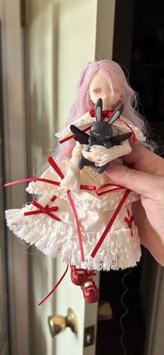 Customer holding the Mahiru BJD action figure. It has long pink hair, a white dress, and holds a black rabbit.