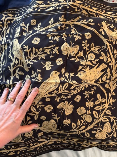 Customer's hand on the Melody Bandana, showing the detailed gold bird print on black fabric.