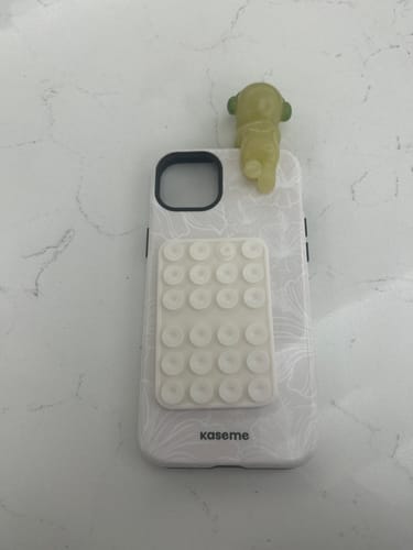 Reviewer's white patterned Impact Case with a suction grip and small decorative figure attached by the user.