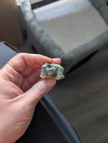 Customer holding a raw, multicolored monthly crystal showing green and dark shades.
