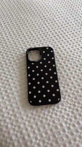 Customer's black Tuxedo Dot iPhone Case with white polka dots, lying on a white textured surface.