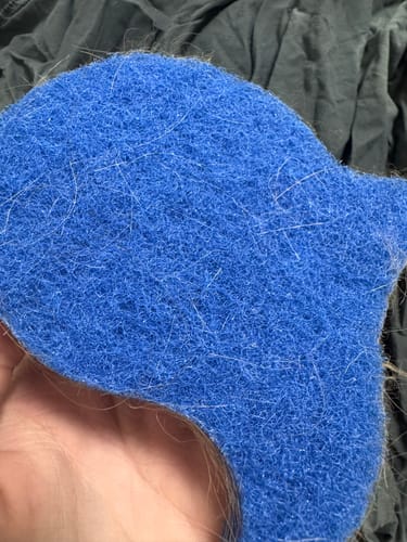 Customer holding a blue Laundry Pet Hair Removal Fish covered in white pet hair after use.