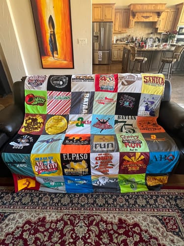 Customer's colorful Project Repat t-shirt quilt made from running shirts, displayed on a black sofa.