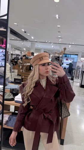 Reviewer in a store wearing the burgundy Vegan Leather Cropped Trench Jacket styled with a tan hat.