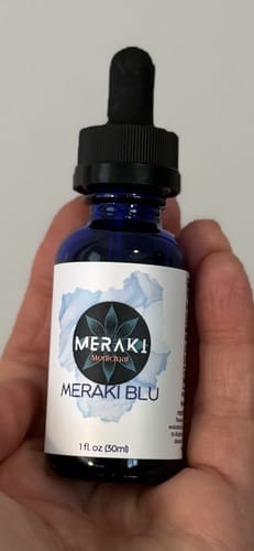 A reviewer holds the small, blue glass bottle of Meraki Blu Methylene Blue in their hand.
