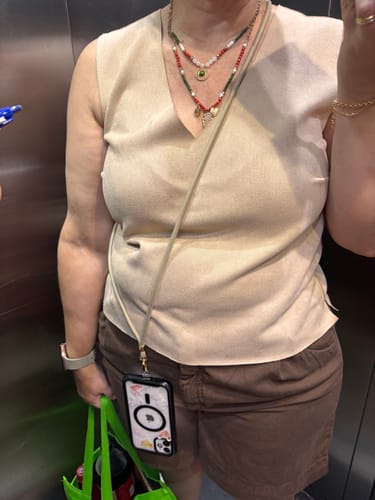 Cliente usando a Alça Universal Areia DOURADA na transversal, com o celular preso ao lado do corpo.