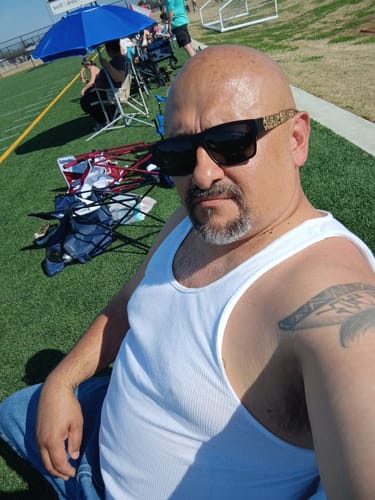 Reviewer sitting outdoors wearing black QUE - Aztec Calendar sunglasses with patterned bamboo temples.