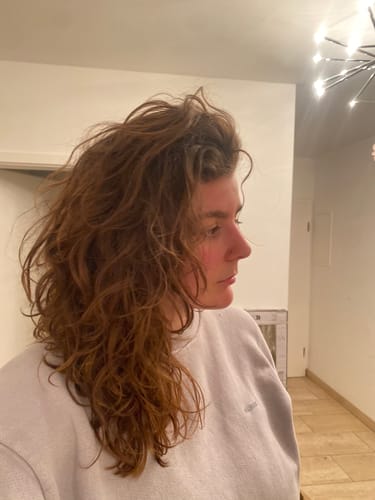 Kundin zeigt ihr welliges, voluminöses Haar nach der Anwendung der Ylang-Ylang-Glow Haarseife.