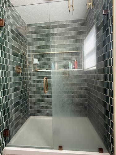 Reviewer's glass shower door, half sparkling clean and half hazy, showing the cleaner's results on soap scum and grime.