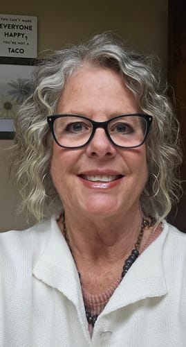 Reviewer smiling while wearing the Bel Koz Single Strand Clay Necklace with a white jacket over a pink sweater.