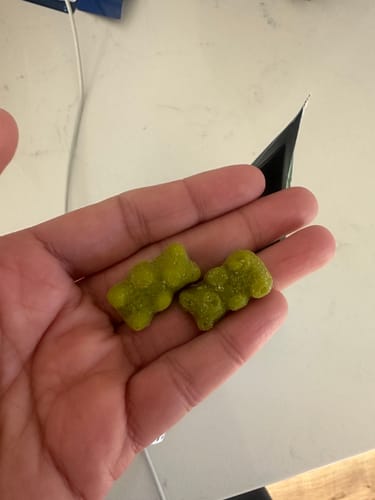 Customer's hand holding two green, bear-shaped NeuroBrocc Gummies for Kids.