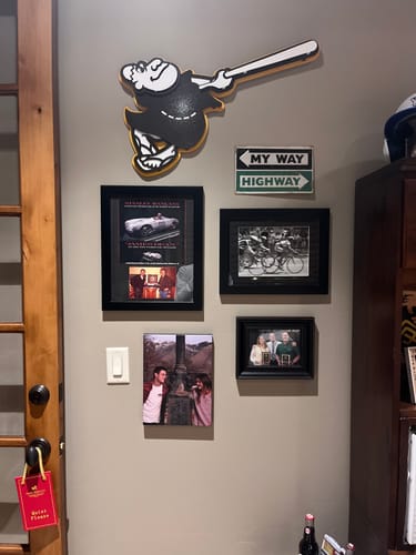 Reviewer's "Swinging Friar" 3D wall art on display in their office above other framed pictures.