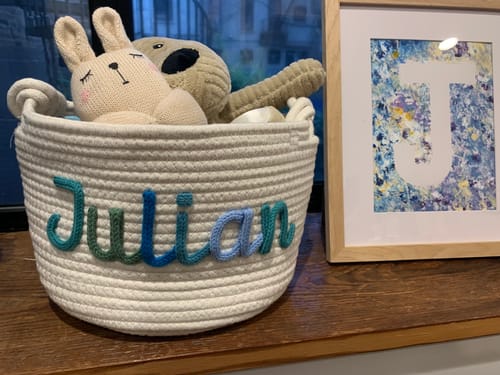 Customer's personalized knitted basket with the name 'Julian' in multicolor yarn, holding toys on a wooden surface.