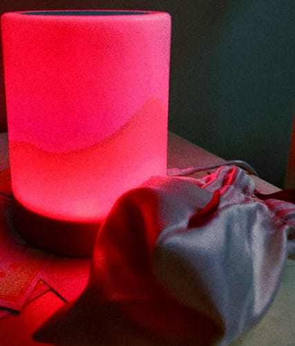 Reviewer's Lem Clitoral Massager glowing pink on a surface next to its satin storage bag.