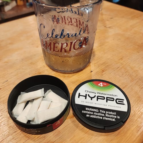 Customer's open can of HYPPE Chewy Watermelon 4mg moist nicotine pouches on a wooden table.