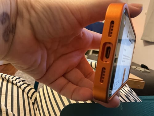 Customer holding the orange MagCase Metal on their phone, showing a close-up of the bottom charging port and speakers.