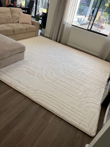 Customer's large, cream-colored Mellow Mat with a carved pattern placed in a modern living room.