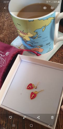 Customer's red Heart & Cross Charm Earrings displayed in their white product box on a table.