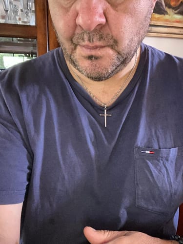 Primer plano de un cliente que lleva el colgante de crucifijo plateado sobre una camiseta azul.