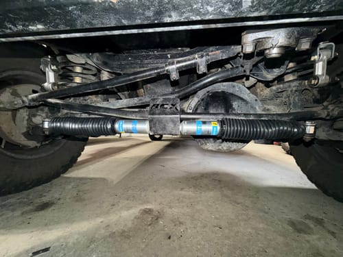 Customer's dual Bilstein 5100 steering dampers installed on the front axle of a truck, viewed from underneath.