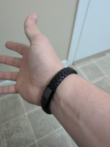 Customer showing the black braided Bracelet fitting on their wrist against a tiled floor.