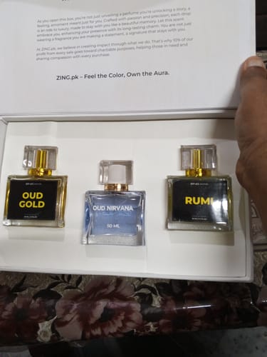 Customer holding the Khushboo-e-Ramzan bundle box open, showing the three oud perfume bottles—Oud Gold, Oud Nirvana, and Rumi.