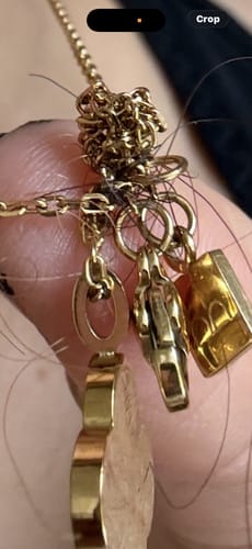 Customer shows the Trust in God Necklace's gold-colored chain badly tangled in a knot with their hair.
