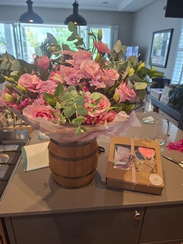 Customer's lush Country Garden Bouquet with pink flowers and foliage in a barrel vase on a counter.