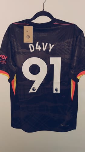 Client montrant le dos de son maillot Chelsea noir personnalisé avec le nom 'D4VY' et le numéro '91'.