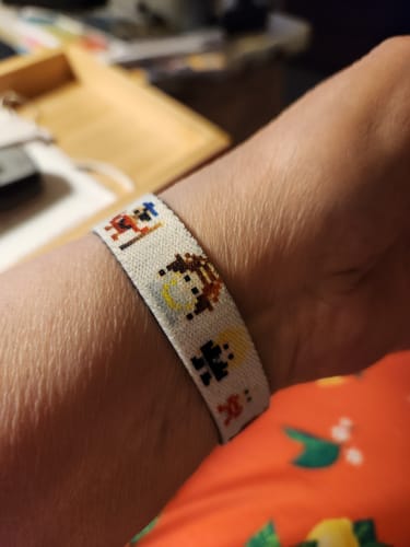 Close-up of a reviewer wearing the fabric Should You Need Us Labyrinth Bracelet, showing the pixel art characters.